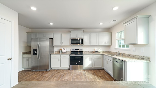 kitchen featuring sink, appliances with stainless steel finishes, white cabinetry, light stone countertops, and light wood-type flooring