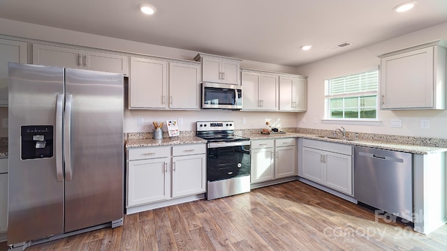 kitchen with stainless steel appliances, wood-type flooring, sink, and white cabinetry