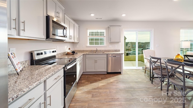 kitchen featuring stainless steel appliances, white cabinetry, sink, and light hardwood / wood-style floors