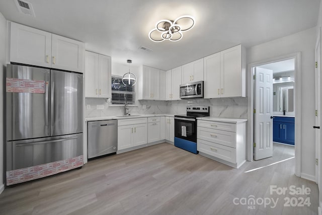 kitchen with white cabinets, hanging light fixtures, backsplash, appliances with stainless steel finishes, and light hardwood / wood-style flooring