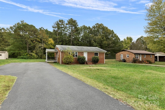 single story home with a storage unit, a front lawn, and a carport