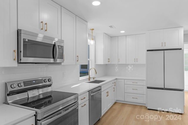 kitchen with appliances with stainless steel finishes, sink, white cabinetry, light hardwood / wood-style floors, and decorative light fixtures