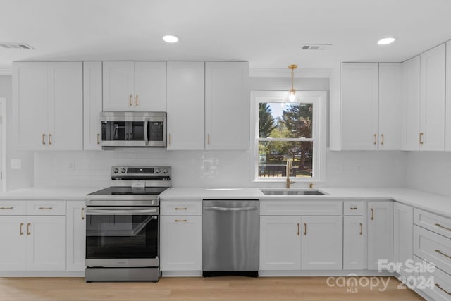 kitchen featuring white cabinets, light hardwood / wood-style flooring, sink, pendant lighting, and stainless steel appliances