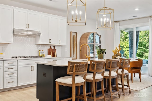 kitchen featuring white cabinets, stainless steel gas stovetop, a kitchen island with sink, light hardwood / wood-style flooring, and decorative light fixtures