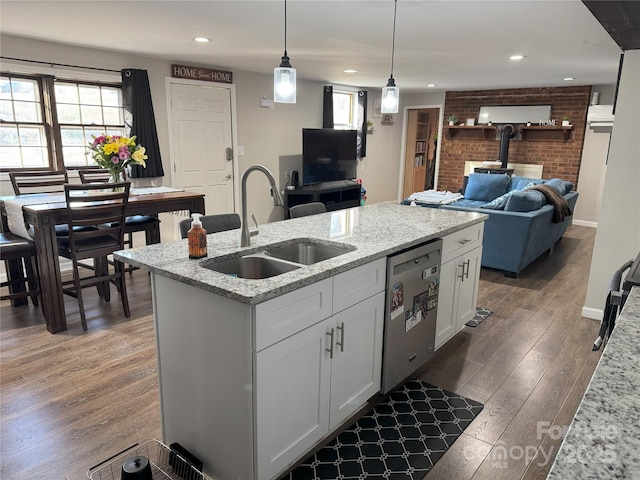 kitchen featuring an island with sink, sink, hanging light fixtures, stainless steel dishwasher, and light stone counters