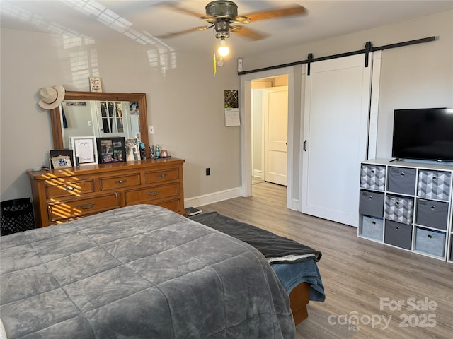 bedroom with hardwood / wood-style flooring, ceiling fan, and a barn door