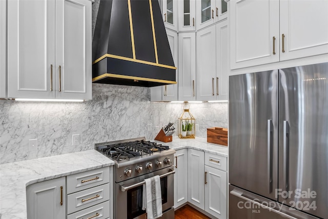 kitchen with backsplash, stainless steel appliances, light stone countertops, and premium range hood