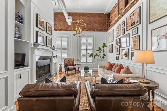 living room featuring wood-type flooring, built in features, crown molding, brick wall, and a chandelier