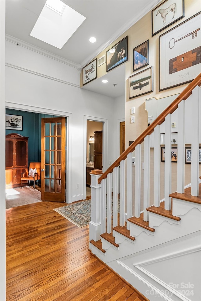 stairs with ornamental molding, hardwood / wood-style floors, and a skylight