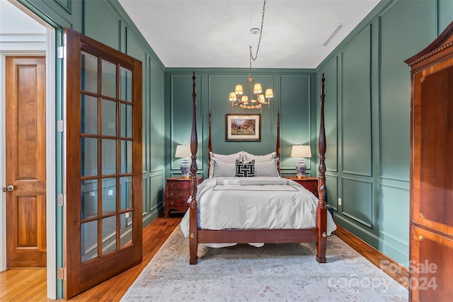 bedroom featuring visible vents, wood finished floors, a notable chandelier, and a decorative wall