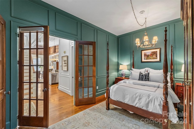 bedroom featuring light wood-style flooring, a decorative wall, french doors, and an inviting chandelier