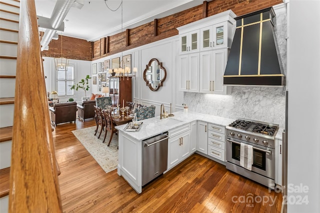 kitchen with white cabinets, light stone counters, appliances with stainless steel finishes, and wall chimney range hood