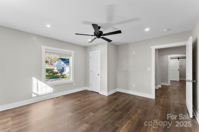 unfurnished bedroom with a barn door, dark hardwood / wood-style floors, and ceiling fan