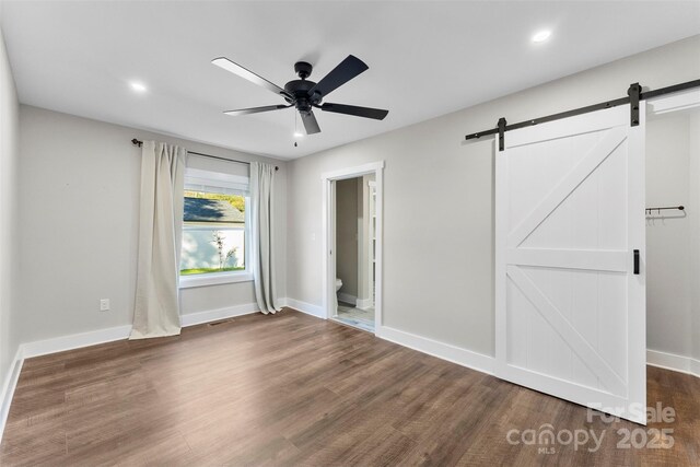 unfurnished bedroom with a barn door, ensuite bath, ceiling fan, and dark wood-type flooring