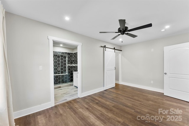 unfurnished bedroom featuring ceiling fan, a barn door, dark hardwood / wood-style flooring, and ensuite bathroom