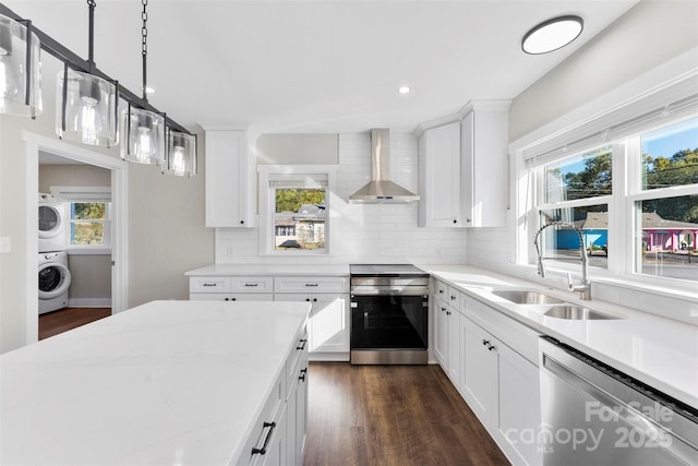 kitchen featuring stacked washing maching and dryer, wall chimney exhaust hood, stainless steel appliances, sink, and white cabinets