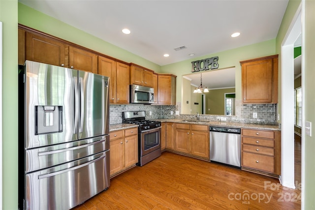 kitchen with hardwood / wood-style flooring, stainless steel appliances, sink, decorative light fixtures, and tasteful backsplash