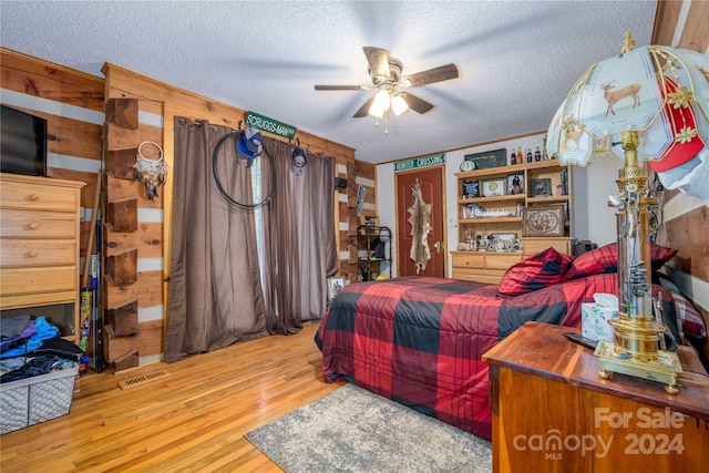 bedroom featuring ceiling fan, a textured ceiling, light hardwood / wood-style flooring, and wooden walls