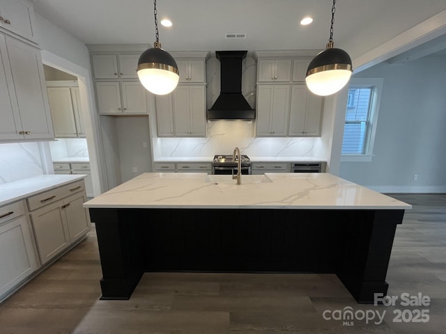 kitchen featuring pendant lighting, a center island with sink, and premium range hood