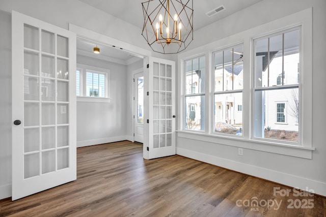 unfurnished dining area featuring french doors, wood-type flooring, and a chandelier