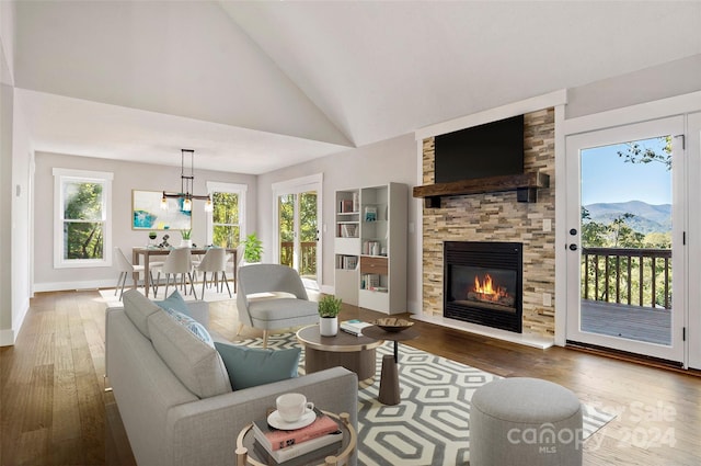 living area featuring hardwood / wood-style floors, a stone fireplace, baseboards, a chandelier, and high vaulted ceiling