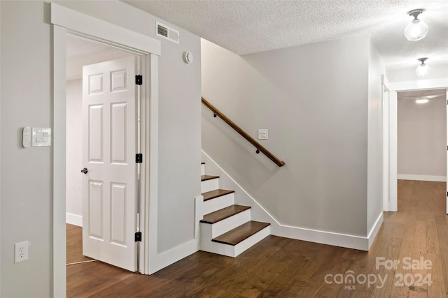 stairway with wood finished floors, a textured ceiling, baseboards, and visible vents