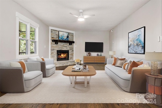 living area with wood finished floors, a textured ceiling, a stone fireplace, and ceiling fan