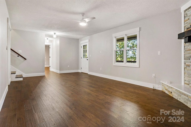 unfurnished living room with dark wood-type flooring, a fireplace, a textured ceiling, and ceiling fan