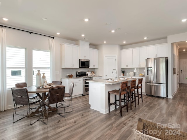 kitchen with stainless steel appliances, wood-type flooring, white cabinetry, and an island with sink