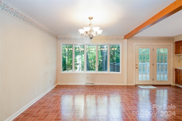 spare room with an inviting chandelier, ornamental molding, french doors, and a wealth of natural light