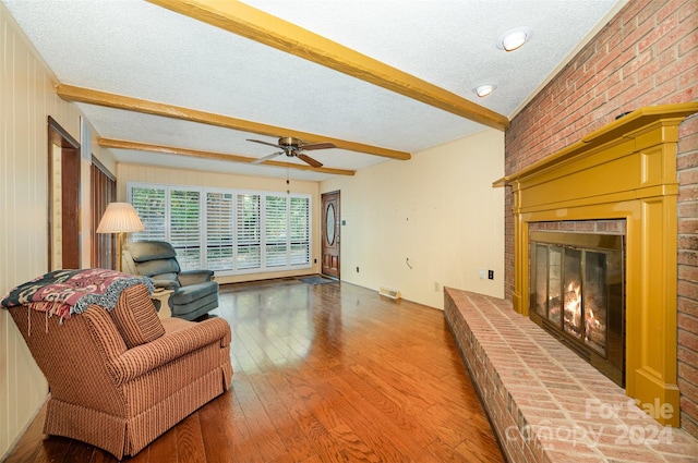 living room featuring hardwood / wood-style flooring, beamed ceiling, a textured ceiling, and a brick fireplace