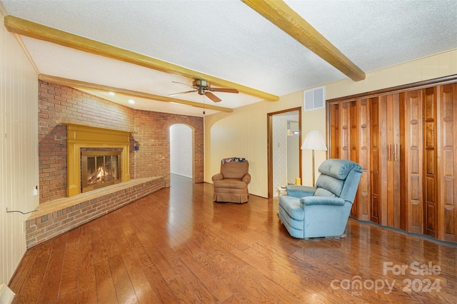 sitting room featuring a fireplace, hardwood / wood-style flooring, beam ceiling, a textured ceiling, and ceiling fan