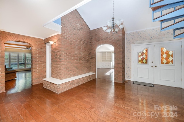 foyer entrance with hardwood / wood-style flooring, high vaulted ceiling, ornamental molding, ceiling fan with notable chandelier, and brick wall