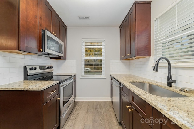 kitchen with sink, stainless steel appliances, light stone counters, light hardwood / wood-style flooring, and decorative backsplash