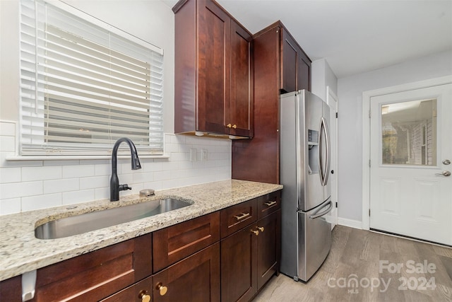 kitchen featuring backsplash, sink, stainless steel refrigerator with ice dispenser, light stone countertops, and light wood-type flooring