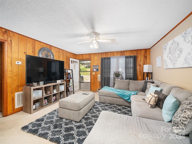 living room featuring wood walls, a textured ceiling, ornamental molding, ceiling fan, and carpet