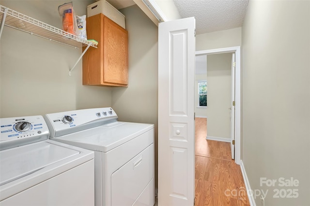 laundry room with a textured ceiling, light wood-style flooring, baseboards, cabinet space, and washing machine and clothes dryer