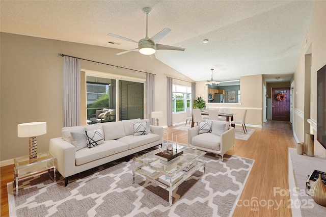 living room featuring lofted ceiling, a textured ceiling, ceiling fan with notable chandelier, visible vents, and light wood-style floors