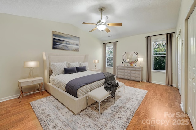 bedroom featuring lofted ceiling, multiple windows, a textured ceiling, and light wood-style flooring