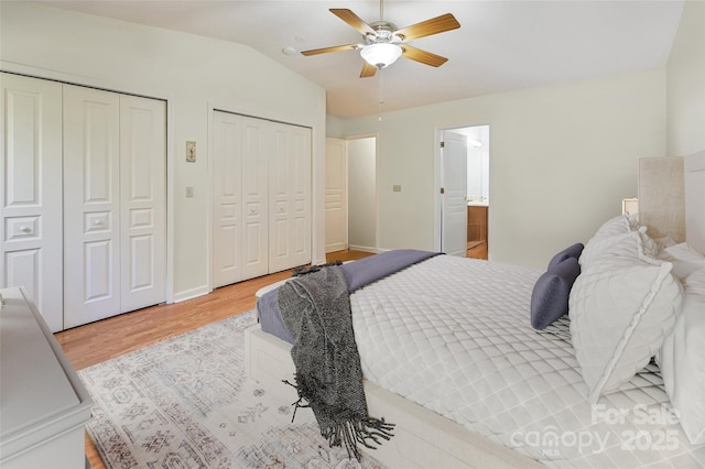 bedroom with multiple closets, lofted ceiling, ceiling fan, wood finished floors, and baseboards