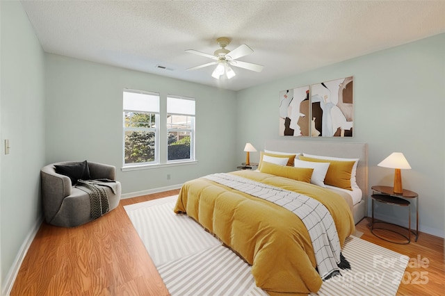 bedroom with a textured ceiling, wood finished floors, a ceiling fan, visible vents, and baseboards