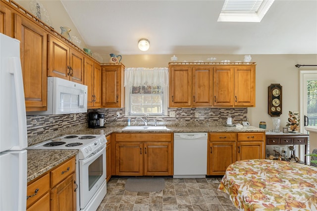 kitchen with decorative backsplash, light stone counters, vaulted ceiling with skylight, sink, and white appliances