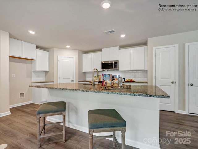 kitchen with dark stone countertops, white cabinets, and an island with sink