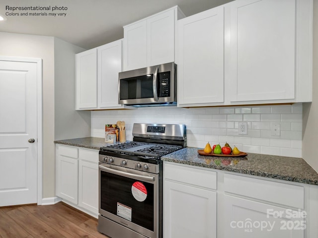 kitchen with white cabinets, dark stone counters, stainless steel appliances, and light hardwood / wood-style floors