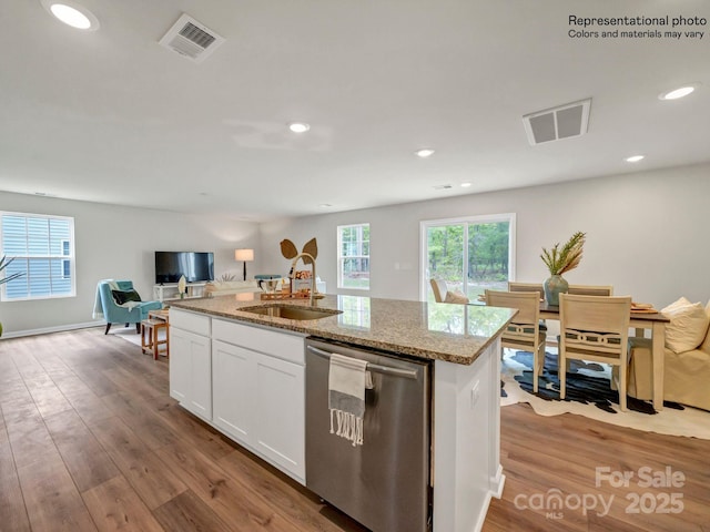 kitchen featuring light stone countertops, white cabinets, sink, stainless steel dishwasher, and a center island with sink