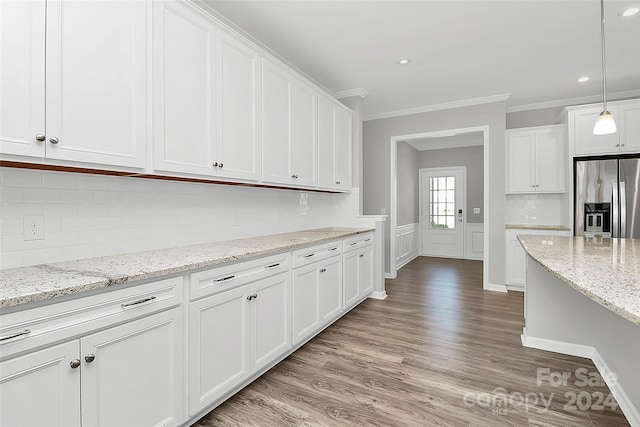 kitchen with stainless steel fridge, white cabinetry, pendant lighting, ornamental molding, and light hardwood / wood-style flooring