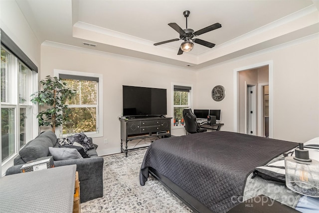 bedroom with ornamental molding, multiple windows, a tray ceiling, and ceiling fan