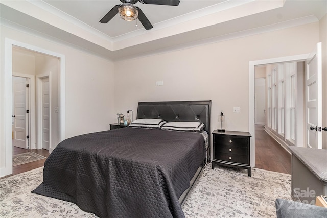 bedroom featuring ornamental molding, wood-type flooring, a tray ceiling, and ceiling fan