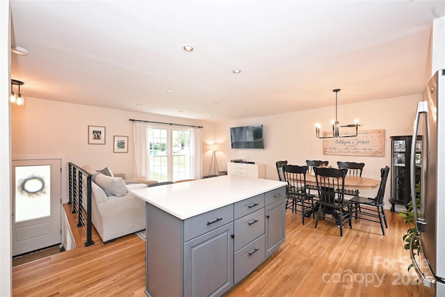 kitchen featuring stainless steel fridge, light wood-type flooring, pendant lighting, gray cabinets, and a kitchen island