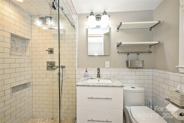 bathroom featuring vanity, toilet, tile walls, and a shower with shower door